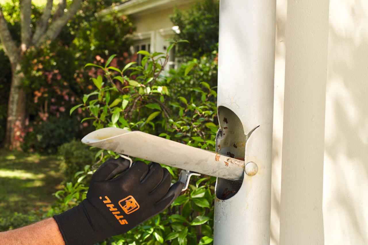 Nahaufnahme, wie eine Person in schwarzen STIHL Schutzhandschuhen die Fallrohrklappe öffnet