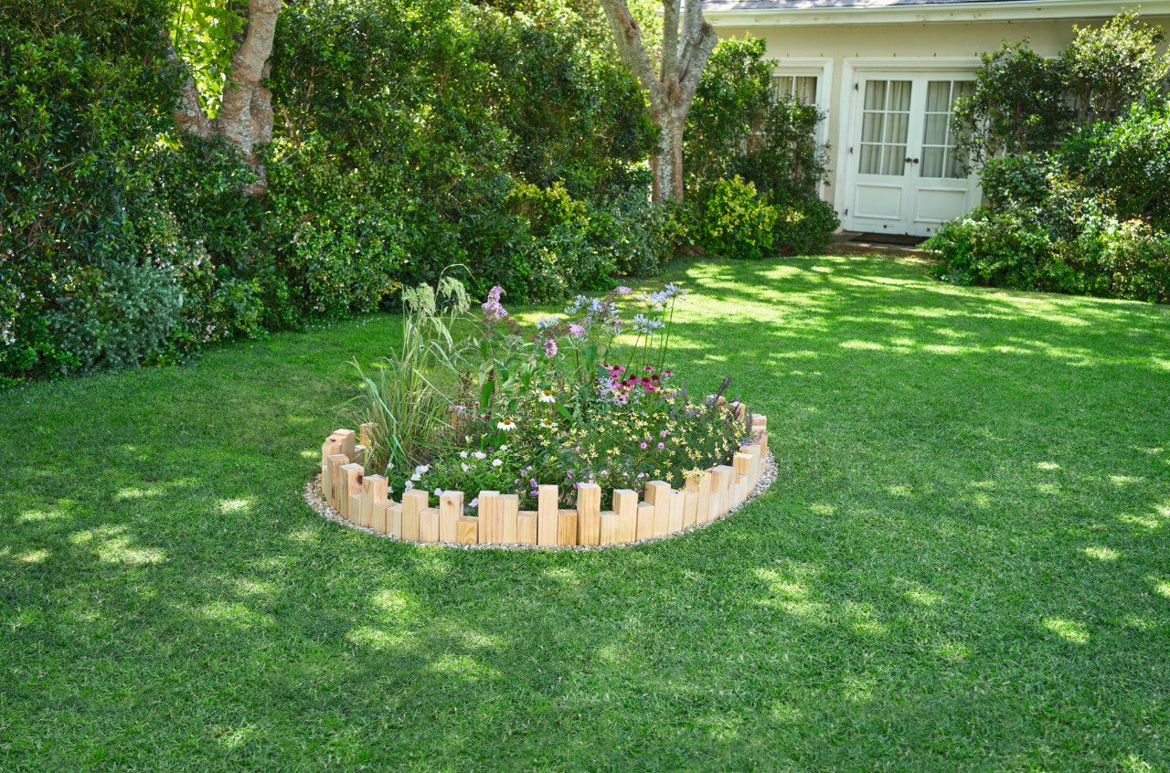 Gartengrundstück mit blühendem Rundbeet im Rasen, umrandet von einer selbstgemachten Beeteinfassung aus Holz