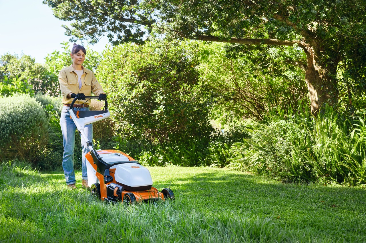 Eine Frau mäht mit einem Akku-Rasenmäher STIHL RMA 448 PV eine Rasenfläche