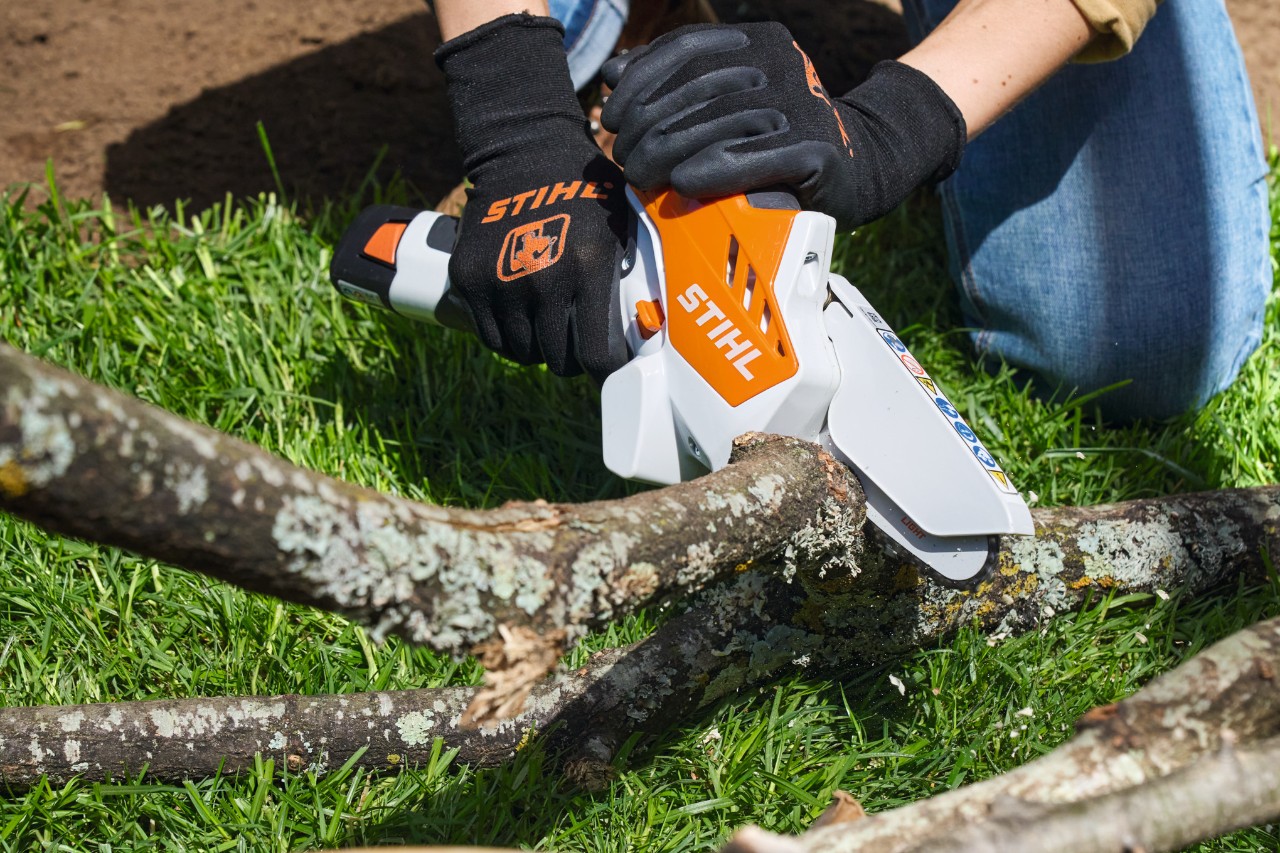 Eine Person mit Arbeitsschutzhandschuhen sägt Äste mit einem Akku-Gehölzschneider STIHL GTA 26 in Stücke