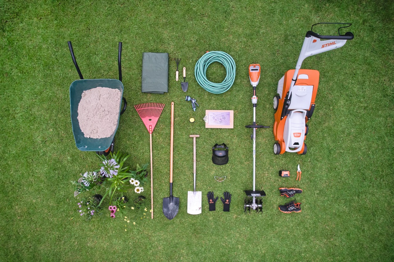 Rasen mit Werkzeugen und Materialien, um ein Inselbeet anzulegen, darunter ein Akku-Rasenmäher STIHL RMA 339 C