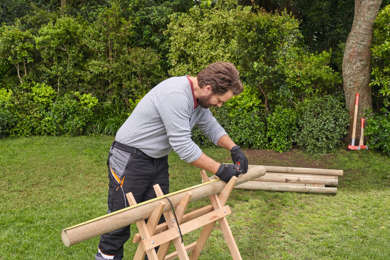 Vor dem Anlegen der Kräuterspirale misst ein Mann Äste auf einem Holzbock aus und kennzeichnet die Längen
