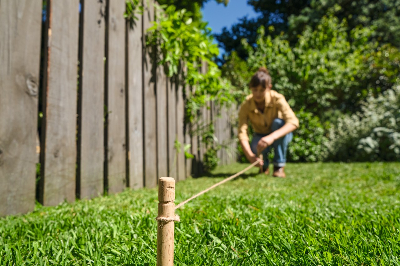 Eine Frau markiert den geplanten Rand des Blühstreifens mit Holzpflöcken und einer Schnur