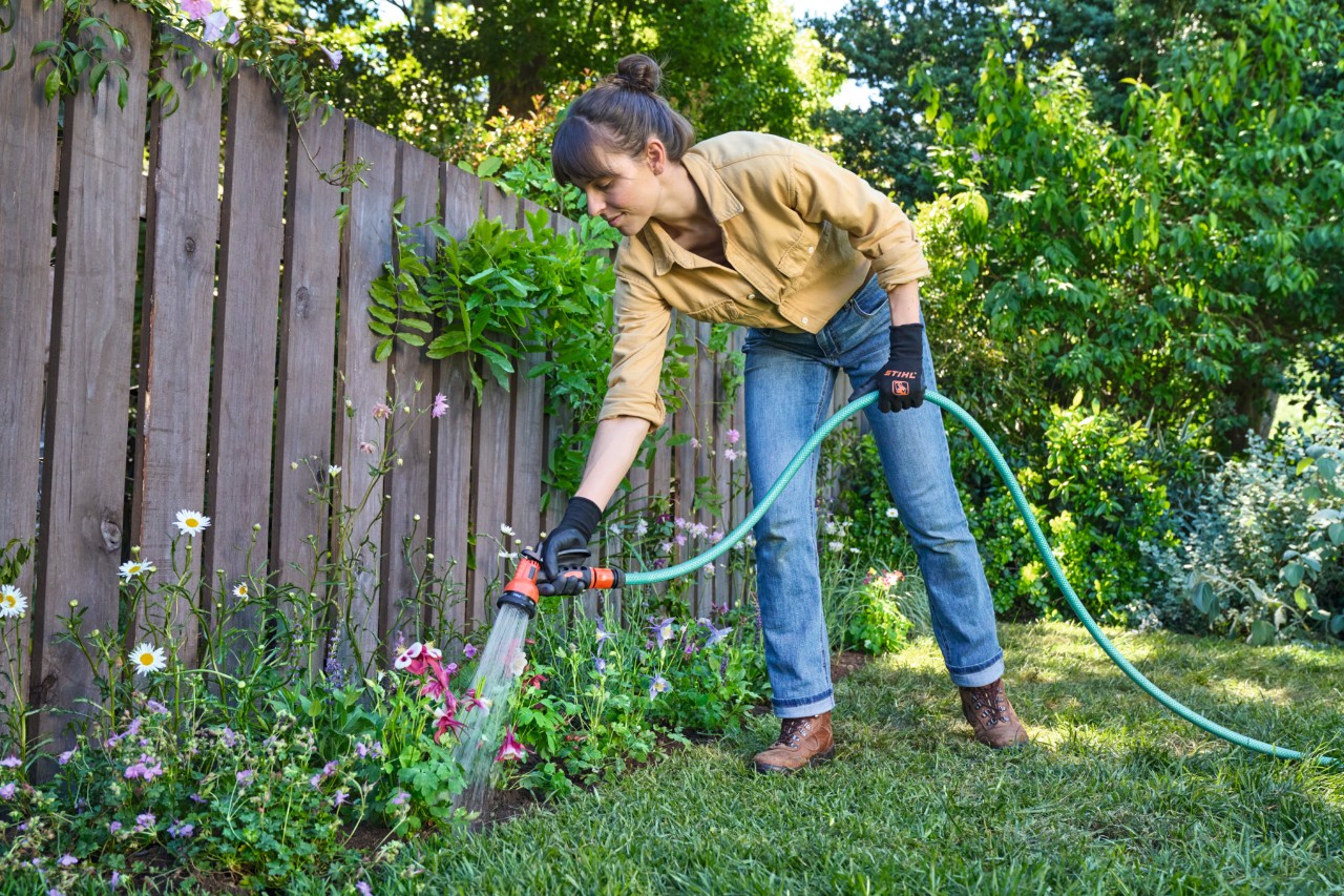 Eine Frau wässert die Blumen auf dem Blühstreifen mit einem Gartenschlauch