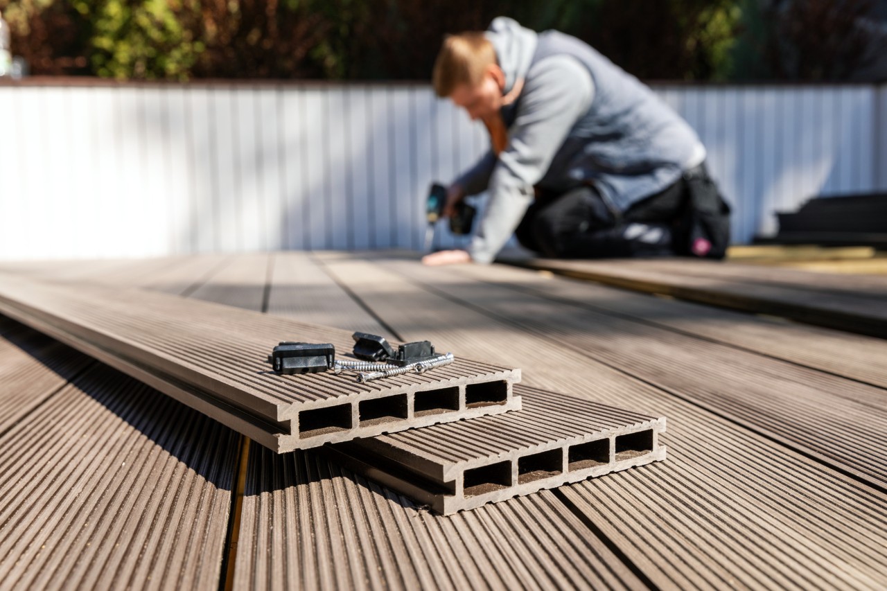 Mann verlegt vor weißem Zaun einen WPC-Boden für eine Terrasse