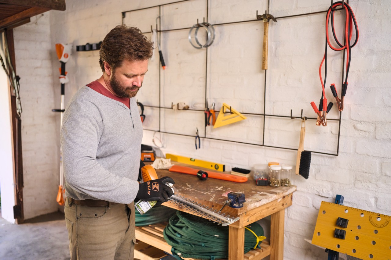 Ein Mann in einer Werkstatt reinigt die Klinge eines Akku-Heckenschneiders STIHL HLA 56 mit Superclean STIHL Spray