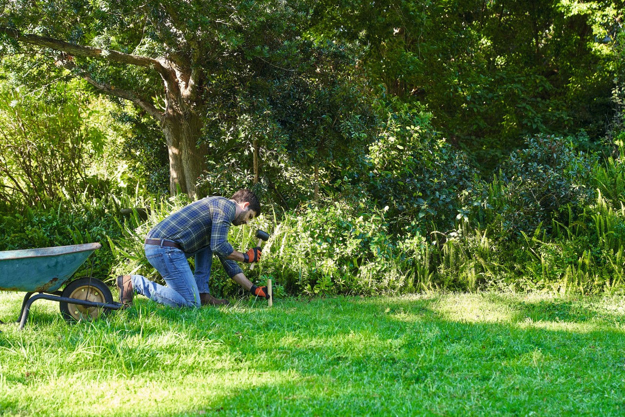 Ein Mann markiert die Fläche zum Anlegen einer Wildblumenwiese mit Wäscheleine und Pflöcken
