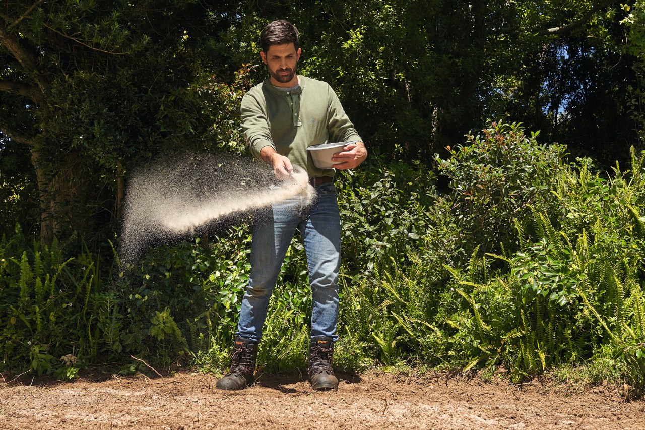 Ein Mann bringt Saatgut für eine Wildblumenwiese aus  