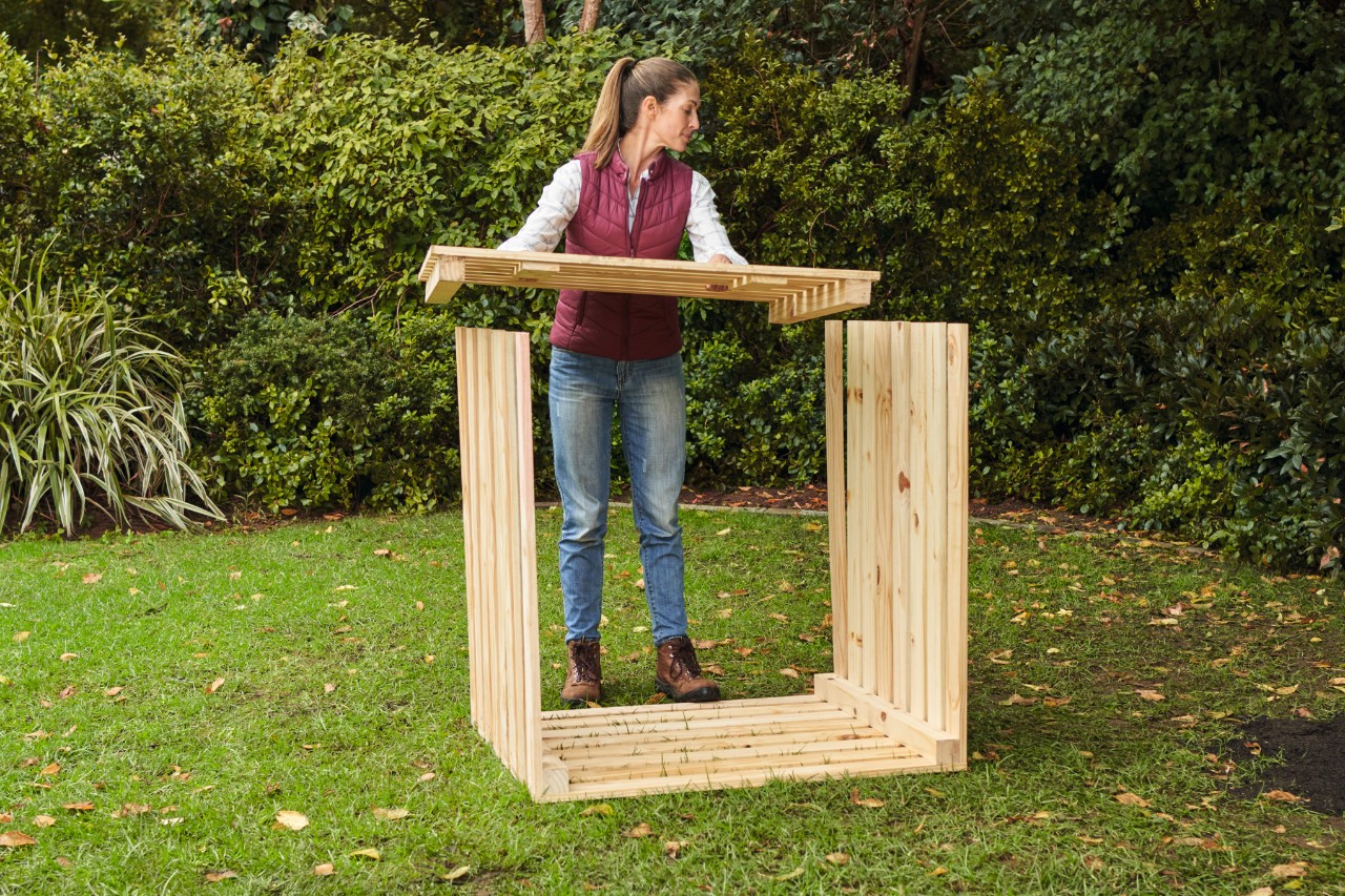Frau auf einem Gartengrundstück legt die Vorderseite für den selber gebauten Komposter passgenau auf die aufragenden Seitenwände