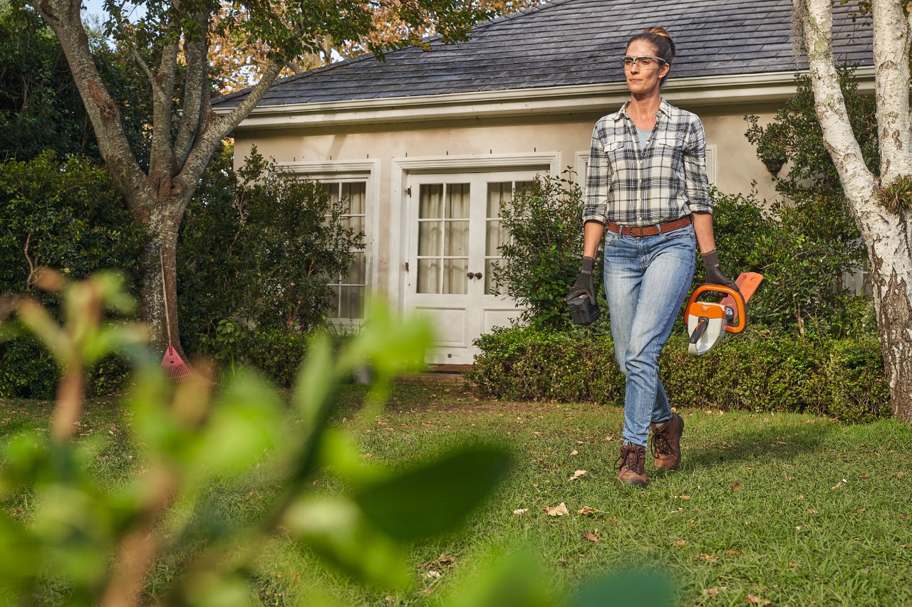 Eine Frau läuft mit einer STIHL Heckenschere über den Rasen vor einem Haus
