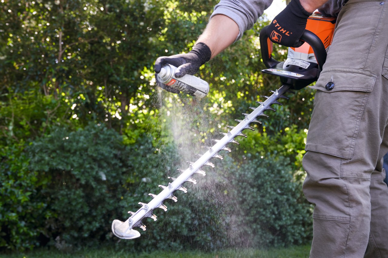 Ein Mann besprüht die Akku-Heckenschere STIHL HSA 60 mit Multiclean