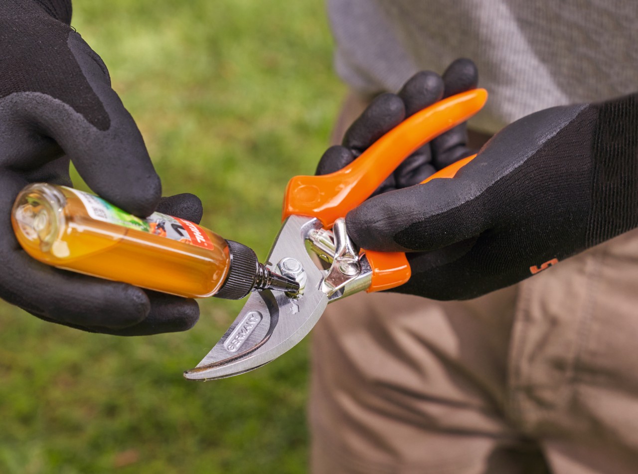 Eine Person mit STIHL Arbeitshandschuhen ölt eine Gartenschere