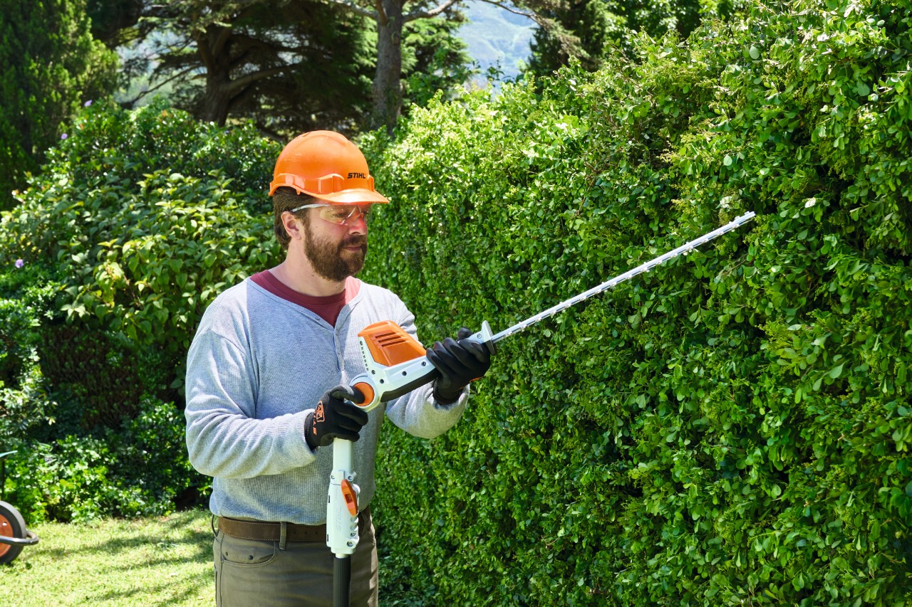Ein Mann in Schutzausrüstung schneidet eine hohe Hecke mit einem Akku-Heckenschneider STIHL HLA 56