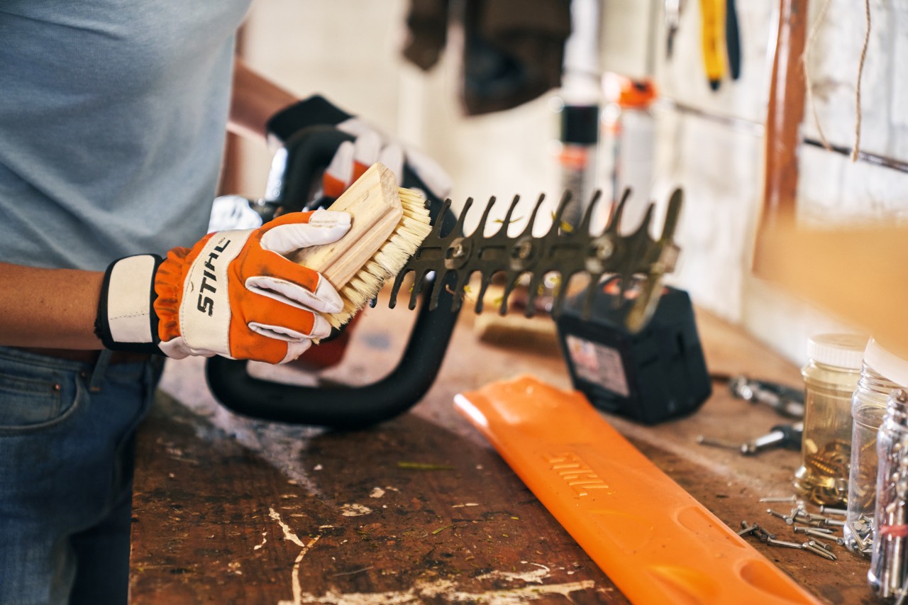 Eine Person reinigt die Akku-Heckenschere STIHL HSA 56 mit einer Bürste in einer Werkstatt 