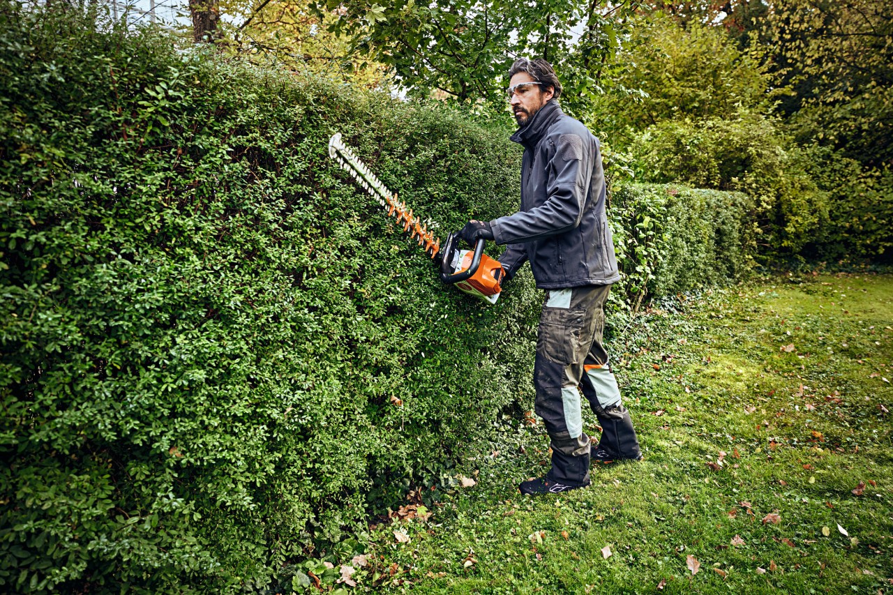 Ein Mann in Schutzausrüstung schneidet mit einem STIHL Heckenschneider eine Hecke