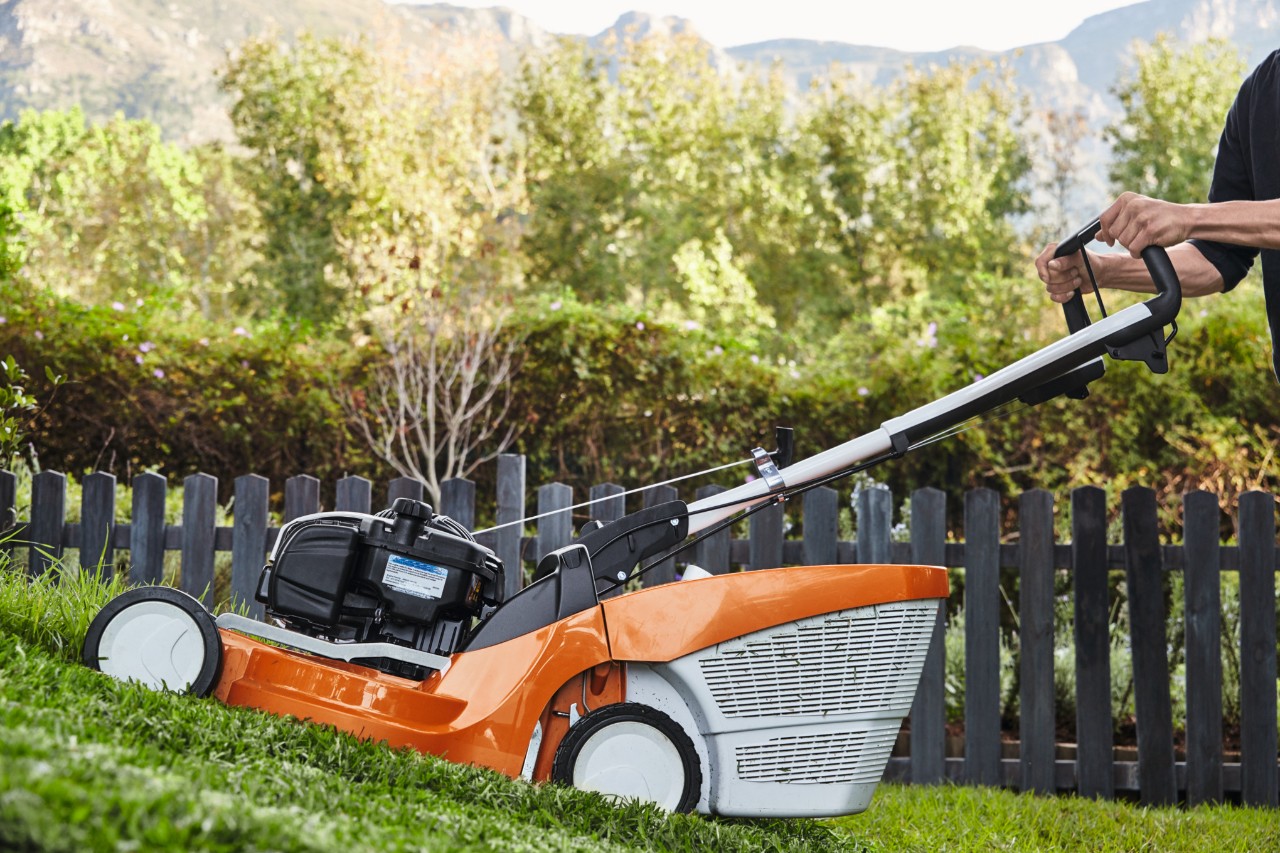Mit einem Benzin-Rasenmäher STIHL RM 448 TC wird entlang eines Zauns ein Hang gemäht 
