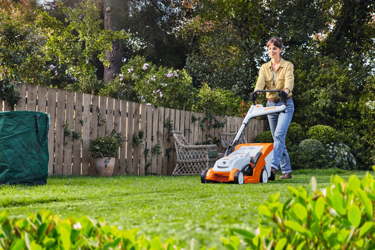 Mann betreibt mit STIHL Akku-Rasenmäher RMA 448 P-C auf einem bewachsenen Grundstück Rasenpflege im Sommer