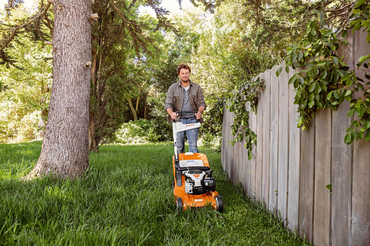 Mann beim Rasenmähen mit STIHL Benzin-Rasenmäher RM 448 TC neben einem Holzzaun