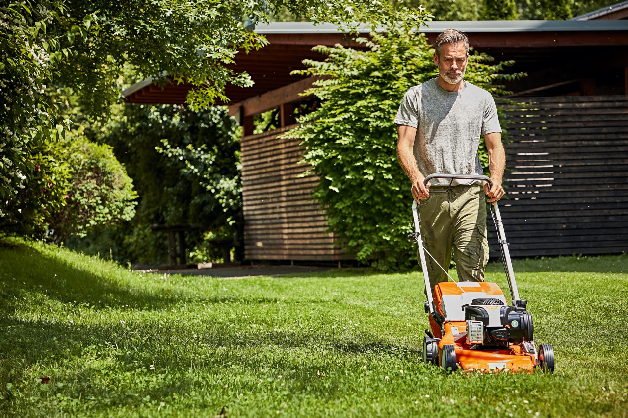 Mann beim richtigen Rasenmähen mit einem STIHL Benzin-Rasenmäher RM 248 vor einer Gartenhütte