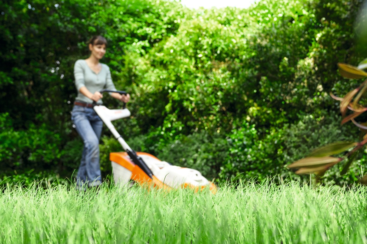Frau mäht den Rasen im Garten