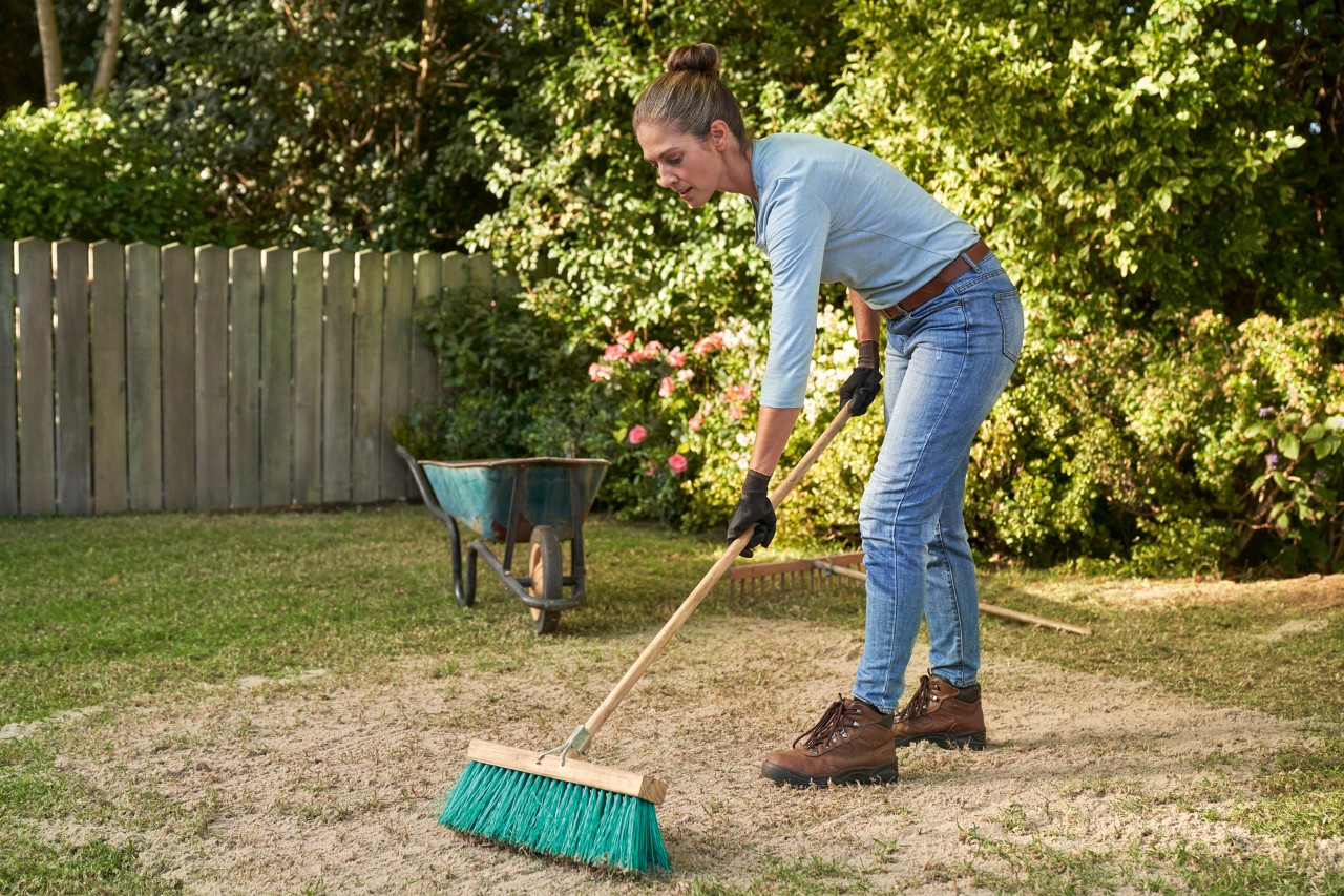Eine Frau mit einem Besen in der Hand ist dabei, den Rasen zu sanden