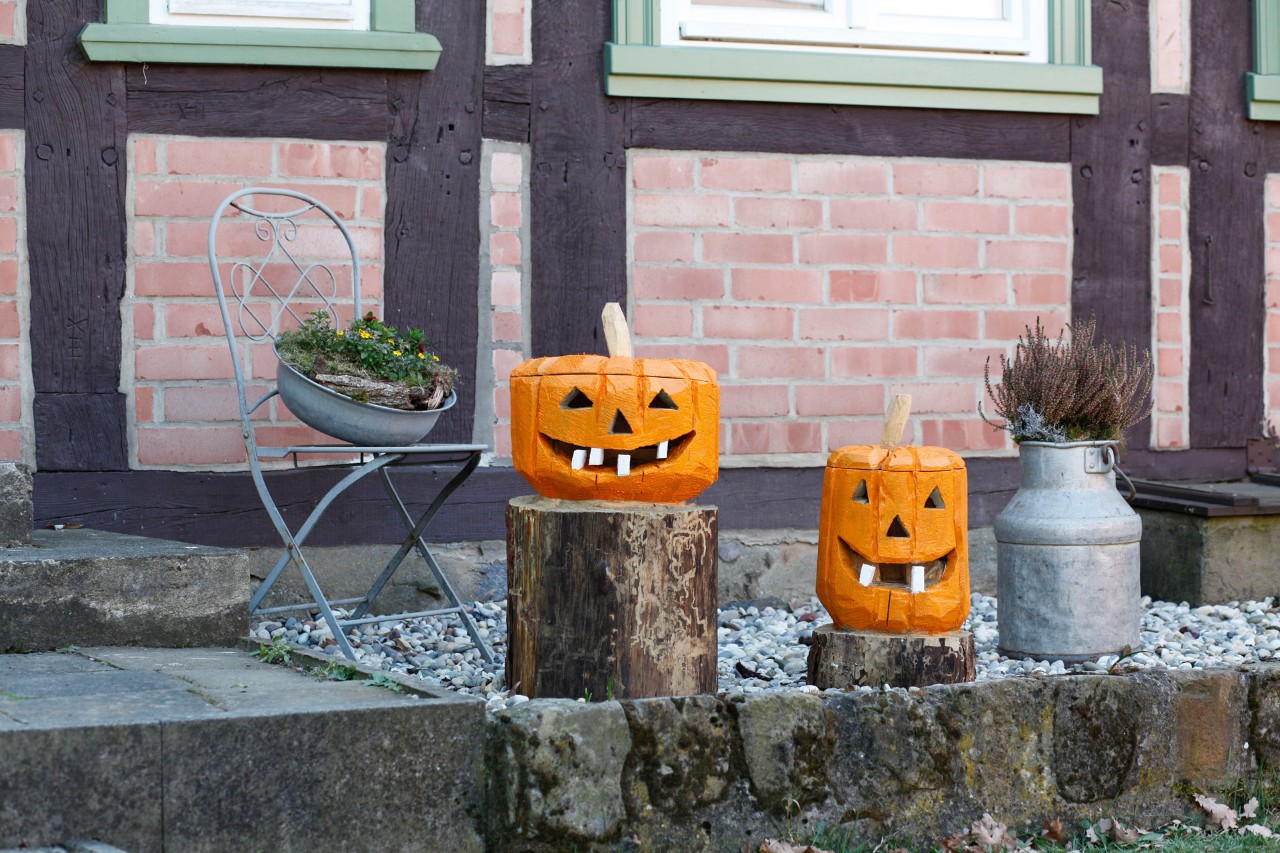 Je ein Kürbis aus Holz zum Selber machen auf zwei Baumstümpfen als Deko vor einem Haus
