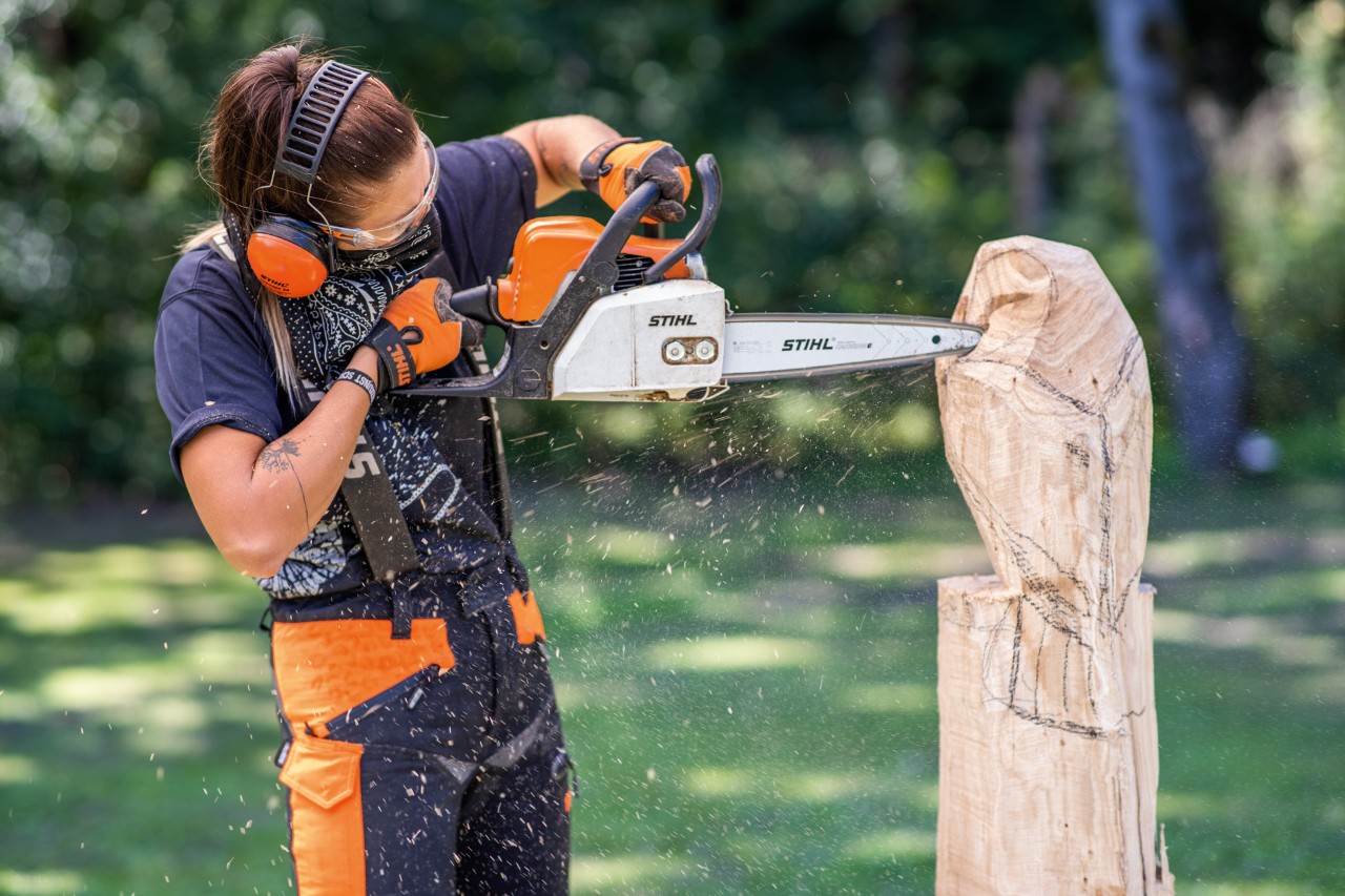 Frau mit STIHL Gehörschutz beim Kettensägenschnitzen einer Eule aus Holz