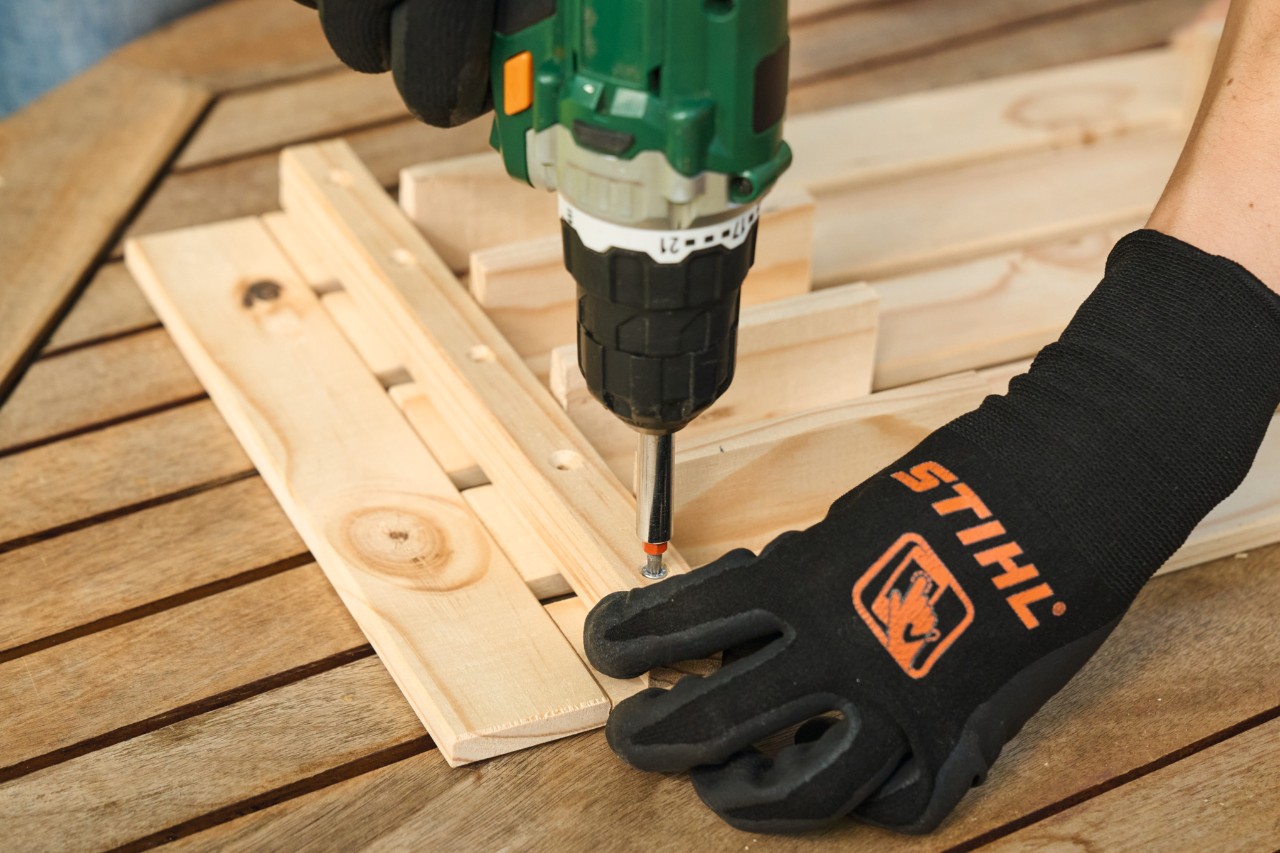Nahaufnahme, wie jemand mit STIHL Schutzhandschuhen Löcher vorbohrt