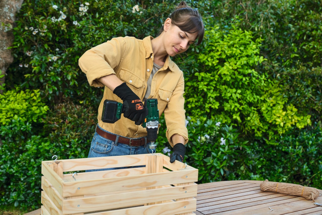 Eine Frau bringt Haken an einem selbstgebauten Blumenkasten an, um ihn später aufhängen zu können 