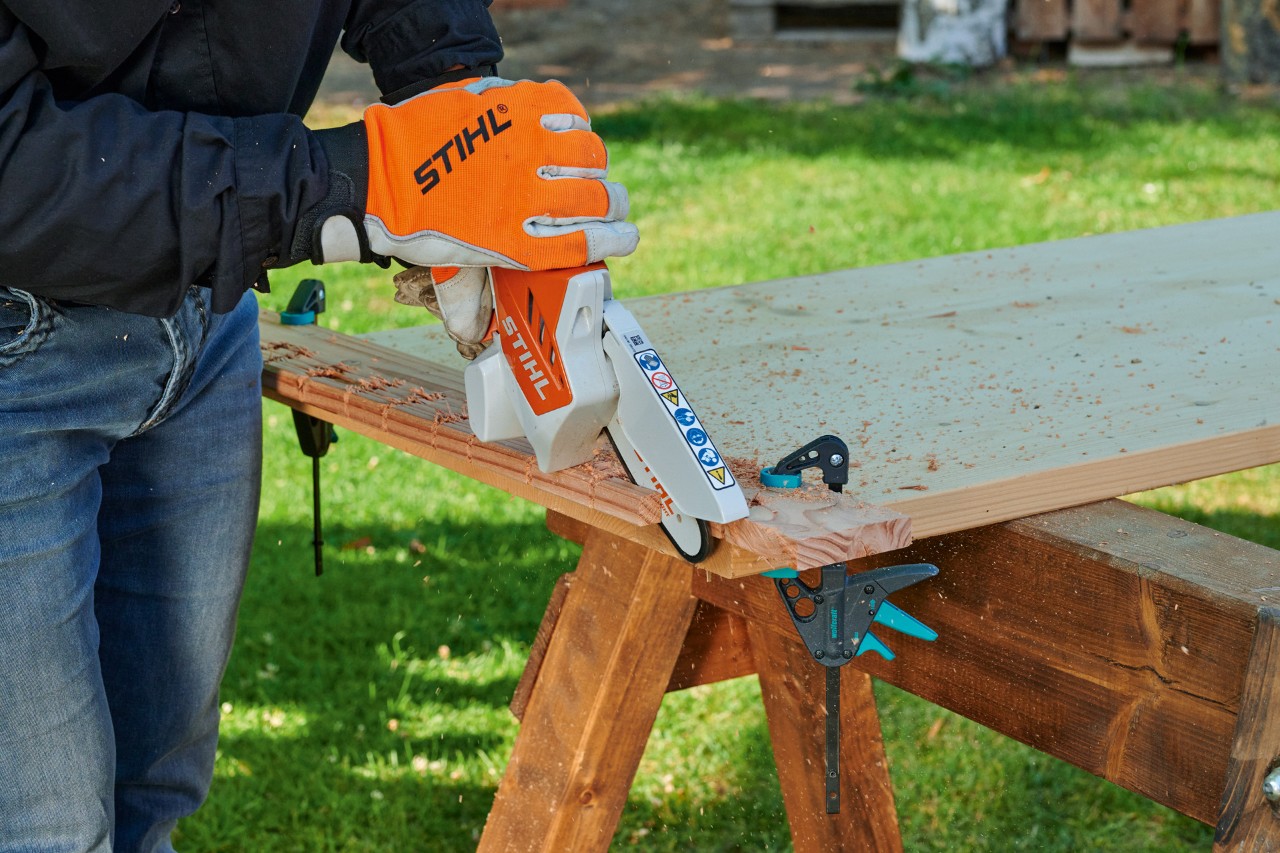  Person zersägt mit STIHL Akku-Gehölzschneider GTA 26 im Garten ein Holzbrett für ein Herz aus Holzabschnitten 