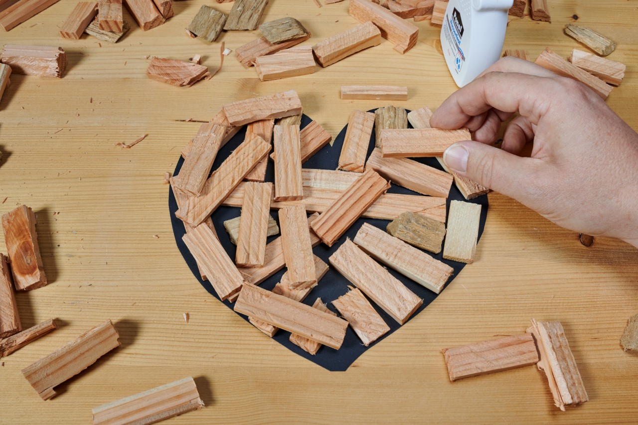 Holzstücke werden auf einem Tisch mit Leim in Form eines Herzes zusammengeleimt. 