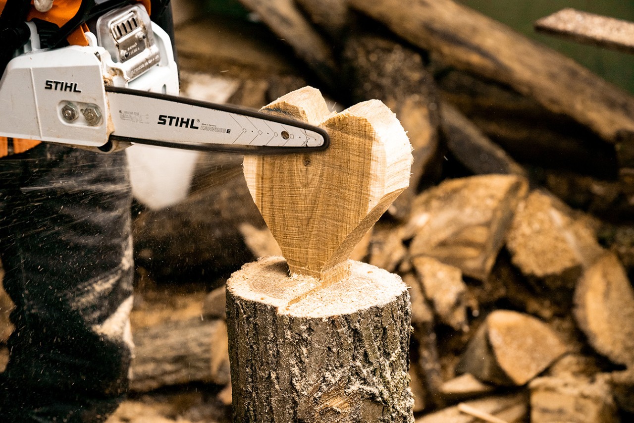Mit einer STIHL Benzin-Kettensäge MS 170 werden die Kanten vom Herz aus Holz geglättet
