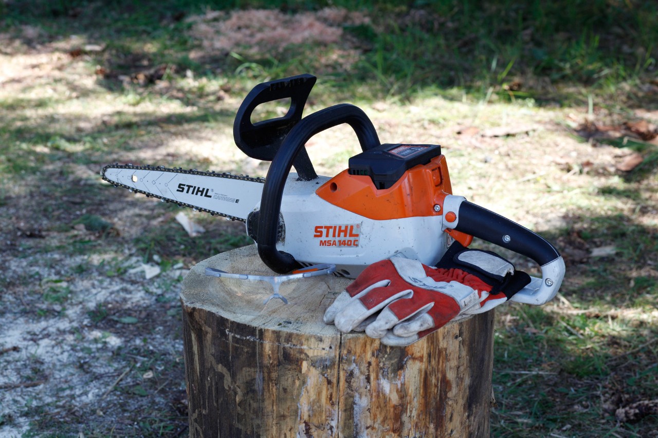 STIHL Akku-Motorsäge MSA 140 C und Schutzhandschuhe liegen auf Baumstumpf bereit, um Kürbis aus Holz selber zu machen