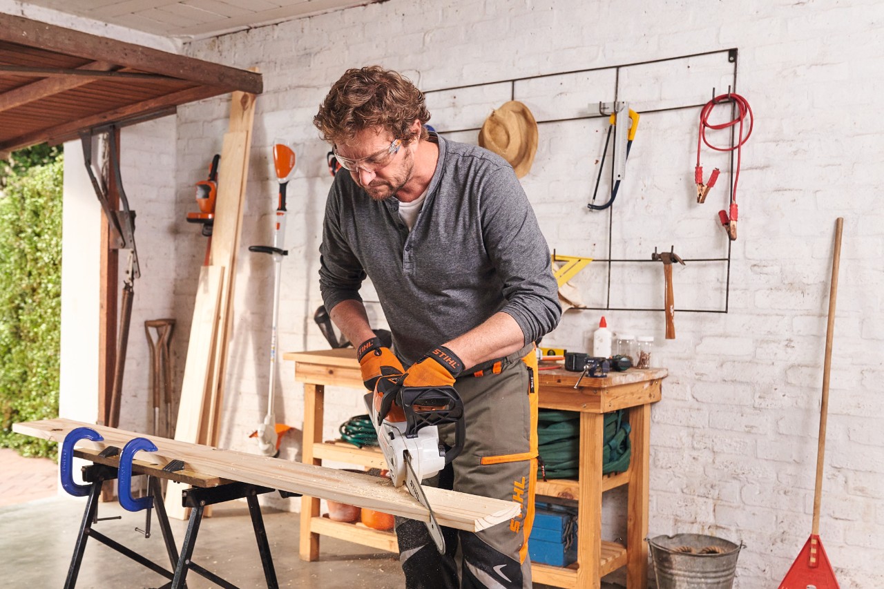 Mann nutzt Akku-Motorsäge STIHL MSA 140 in der Garage, um Brett für ein Pflanzenregal zu sägen