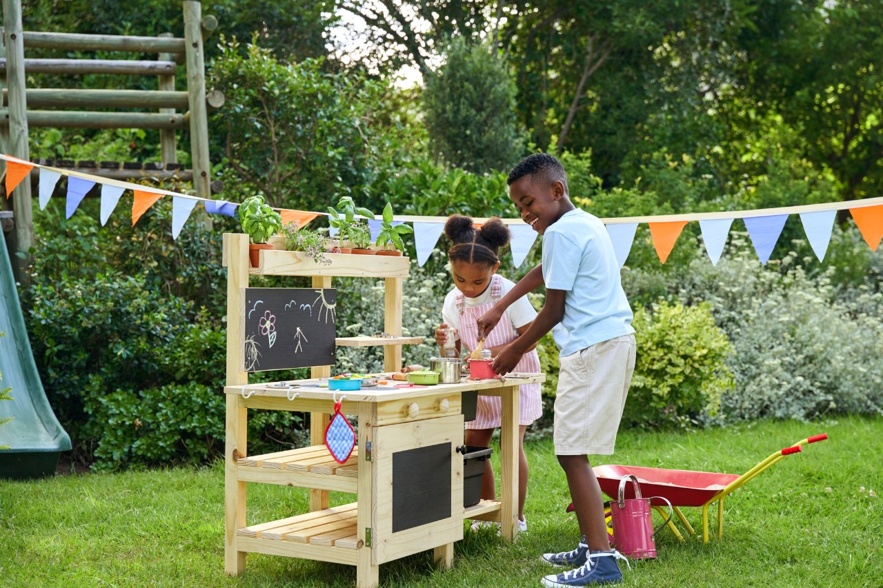 Mädchen und Junge im Garten und beim Kochen in ihrer neuen DIY Matschküche