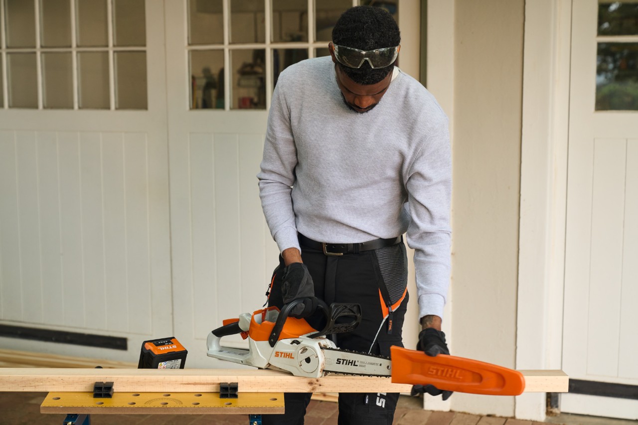Ein Mann vor einer Werkstatt entfernt den Schutz einer Akku-Kettensäge STIHL MSA 70 