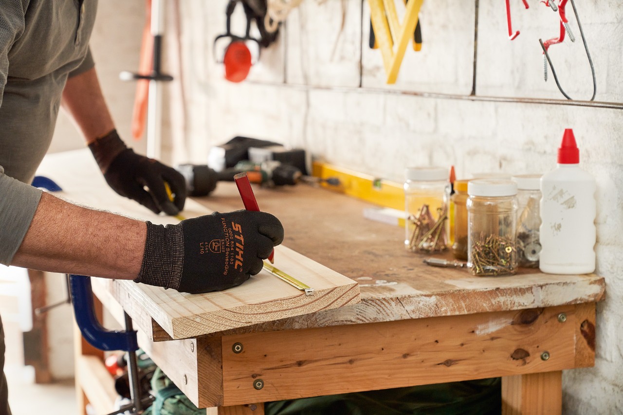 Mann mit STIHL Schutzhandschuhen markiert Bohrlöcher auf einem Holzbrett