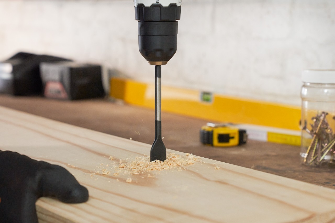 Eine Person bohrt Löcher in ein Holzbrett, um einen Gartengerätehalter selber zu bauen