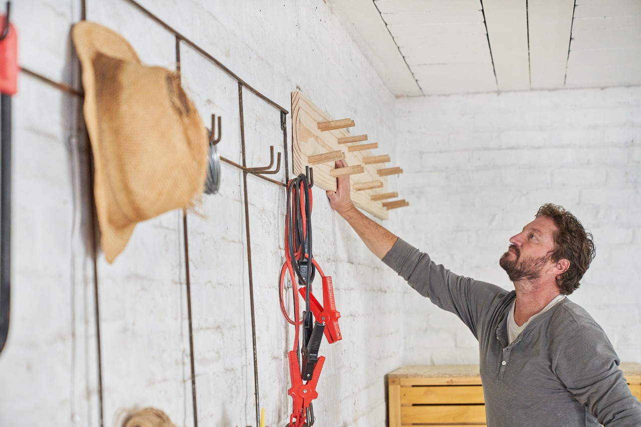 Ein Mann steht vor einem Gartengerätehalter, den er selber gebaut hat
