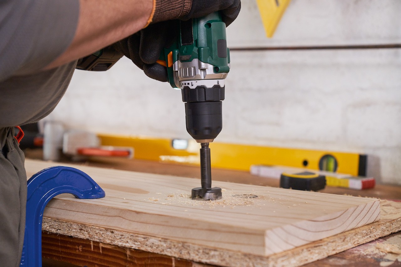 Ein Mann bohrt mit einem Flachbohrer Löcher in ein Holzbrett für einen Gartengerätehalter