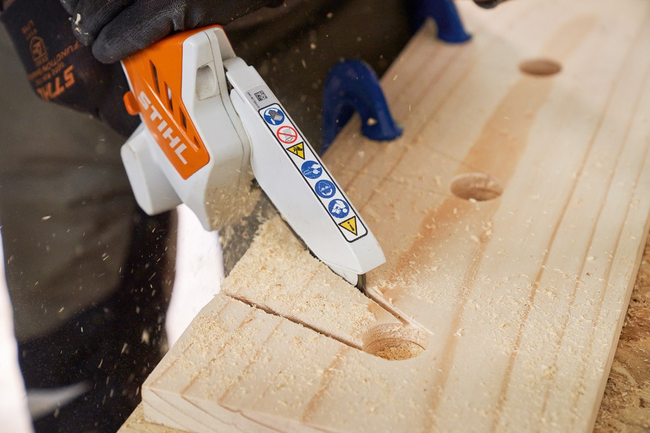 Jemand sägt mit dem STIHL Akku-Gehölzschneider GTA 26 Aussparungen aus einem Holzbrett