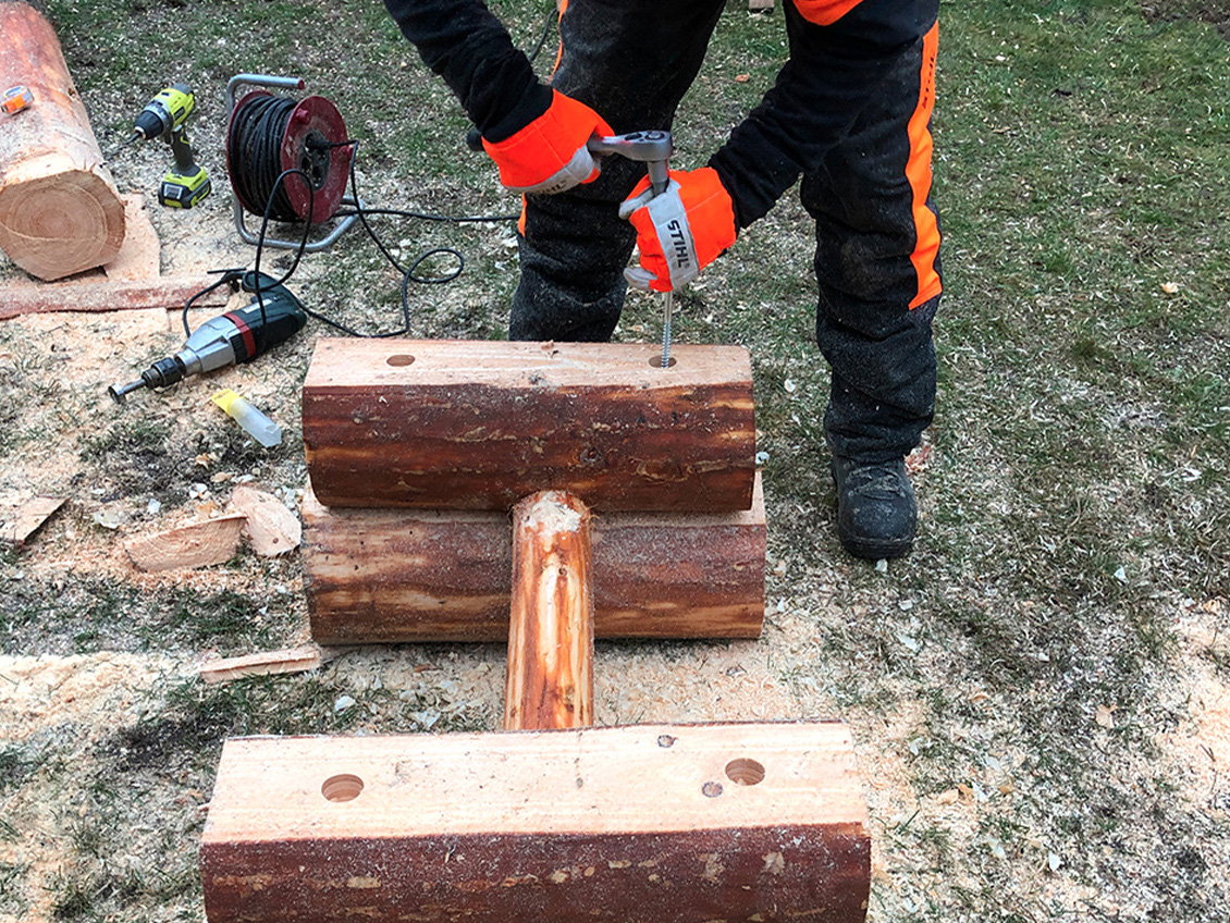 Person in Schutzkleidung montiert die Tischbeine mit Holzschrauben