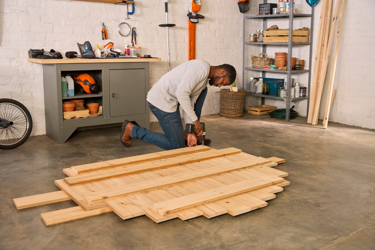 Ein kniender Mann schraubt die Stützplatten mit einem Akku-Schrauber fest.