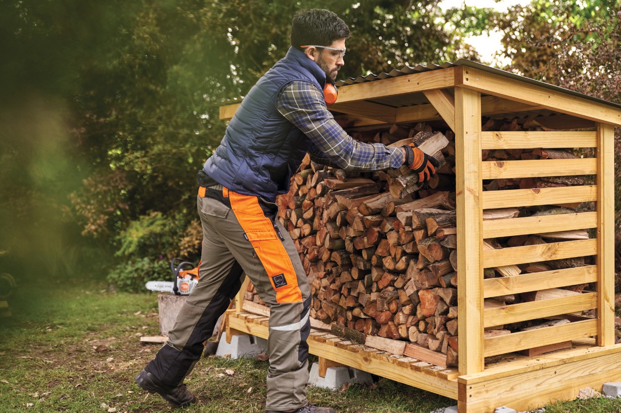 Mann stapelt Brennholz richtig im selbstgebauten Holzunterstand