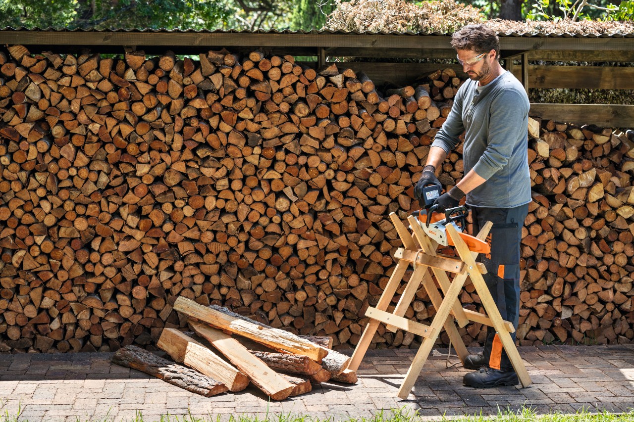 Mann steht vor Brennholz, das in einem Stapel unter einem Dach gelagert wird.