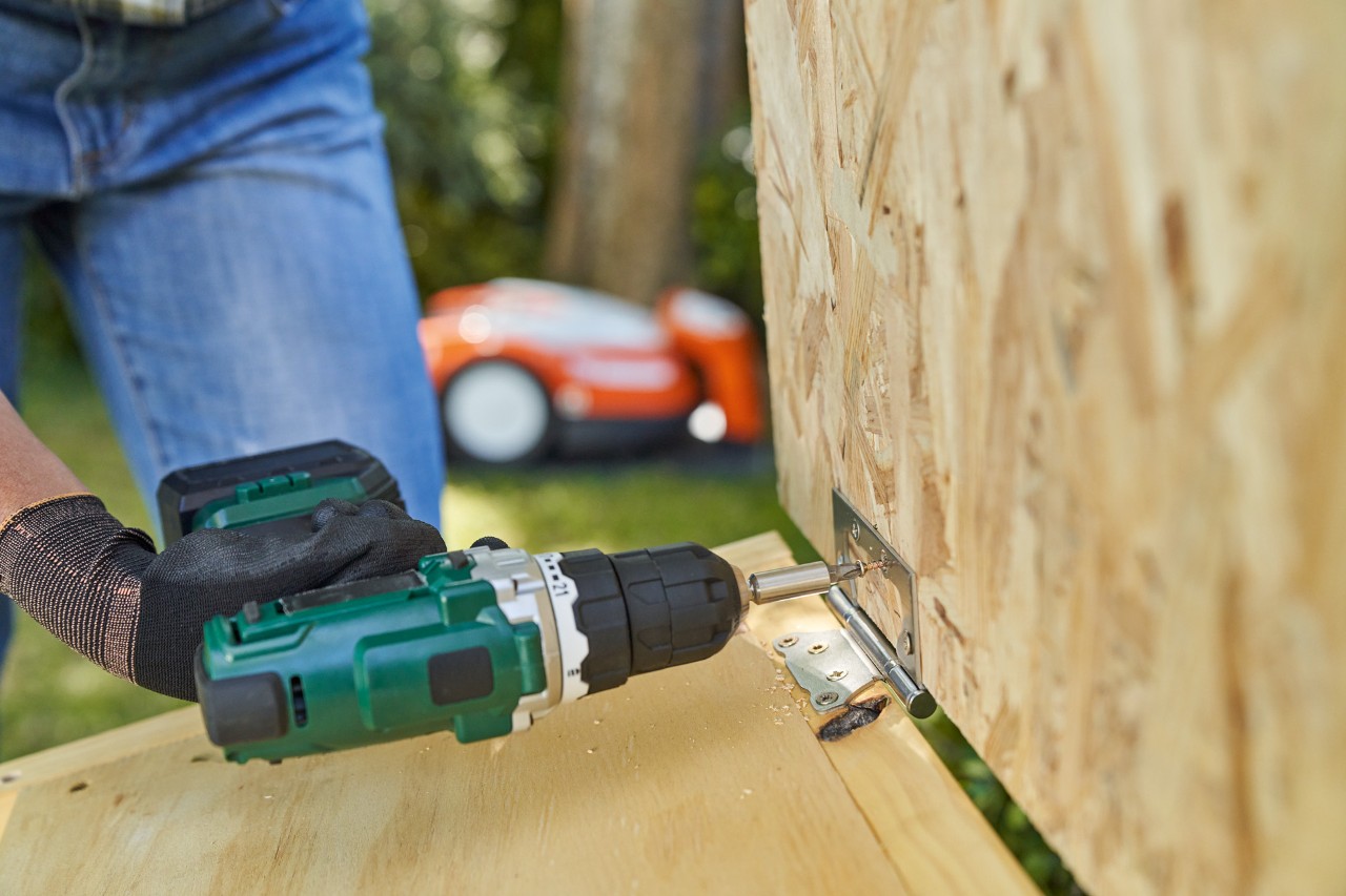 Nahaufnahme: Hand mit STIHL Arbeitshandschuh FUNCTION SENSOTOUCH schraubt Scharniere für Dach der Mähroboter-Garage fest