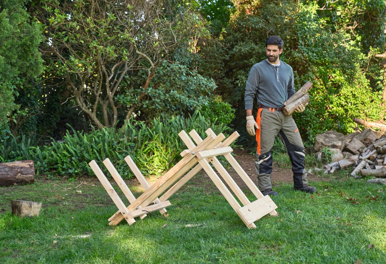 Ein Mann in einem Garten trägt Holzscheite zu einem selber gebauten Sägebock