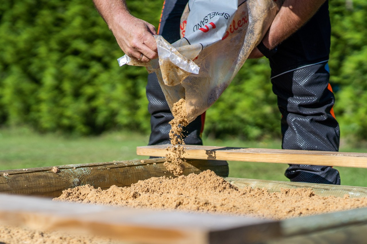 Selbstgebauter Sandkasten wird mit Sand befüllt