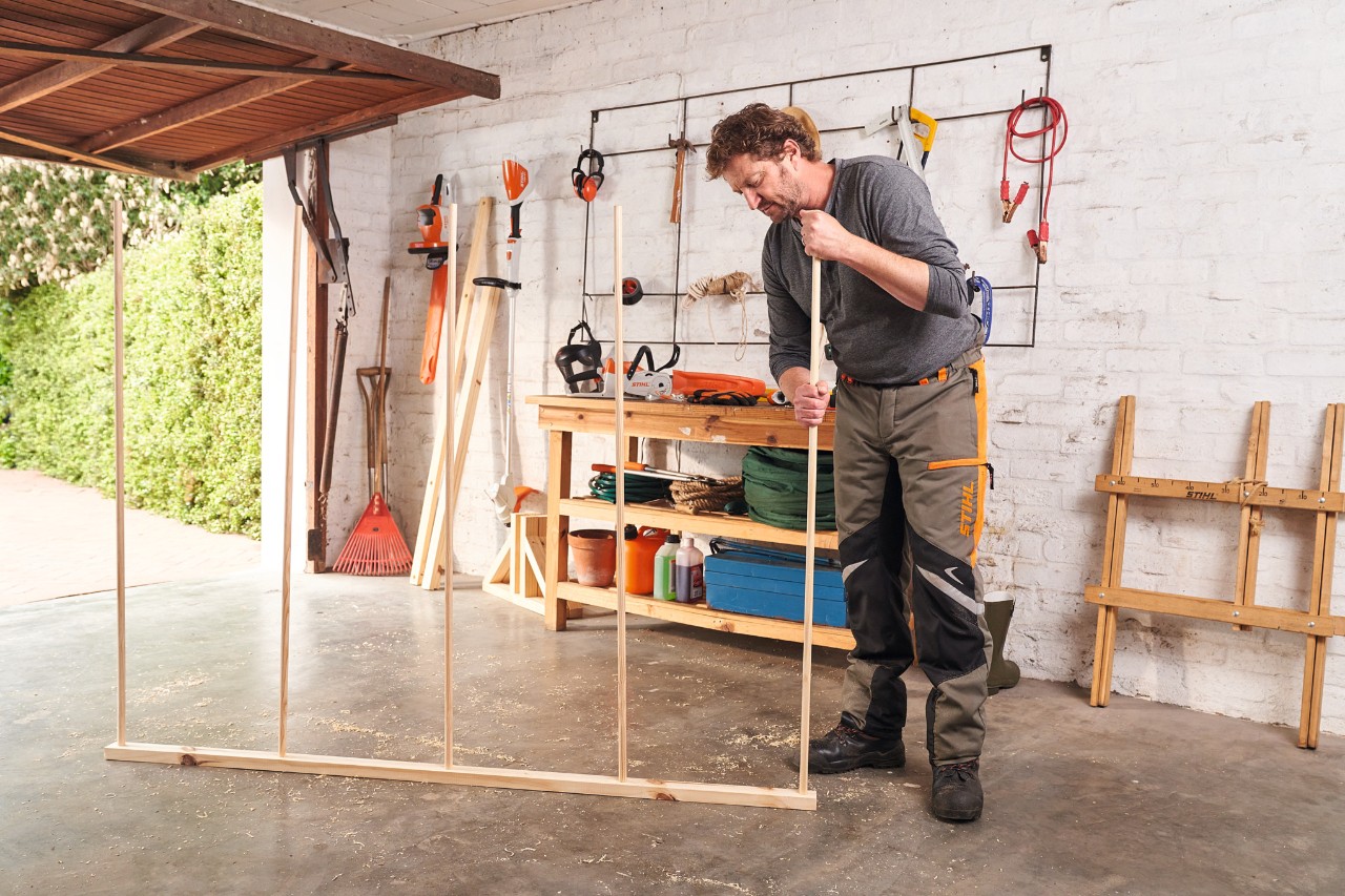 Mann steckt Rundstäbe für einen Sichtschutz aus Holz in einer Garage zusammen