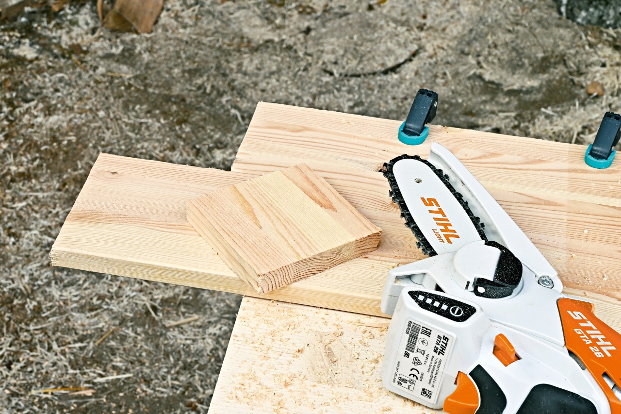 STIHL Akku-Gehölzschneider GTA 26 neben einem Holzbrett, aus dem der Eingang für ein Igelhaus gesägt wurde